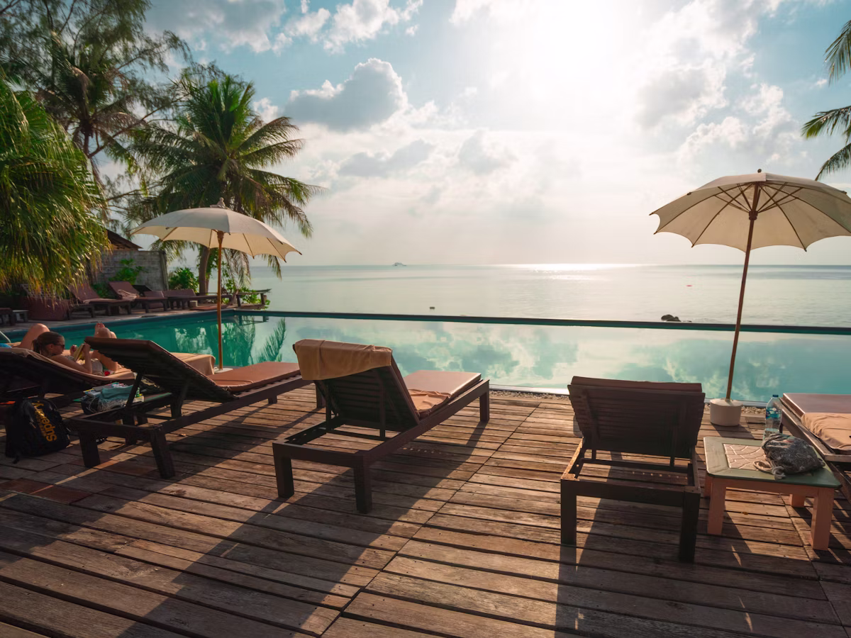 Poolside deck with parasols and sun loungers by calm blue water